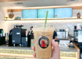 A hand holds an iced coffee in a clear, compostable Complex Brew cup.